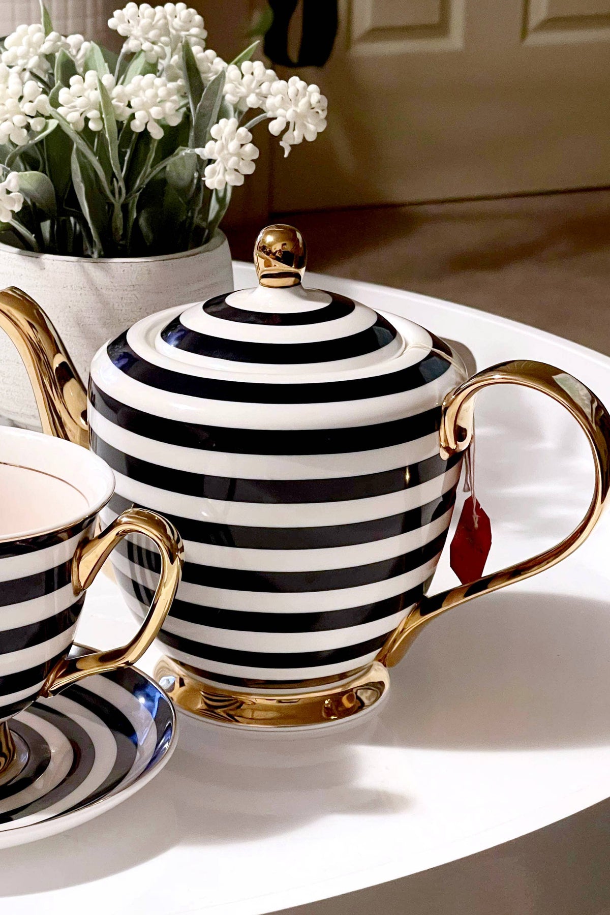 Black and white striped teapot and cup with gold handles on a table.