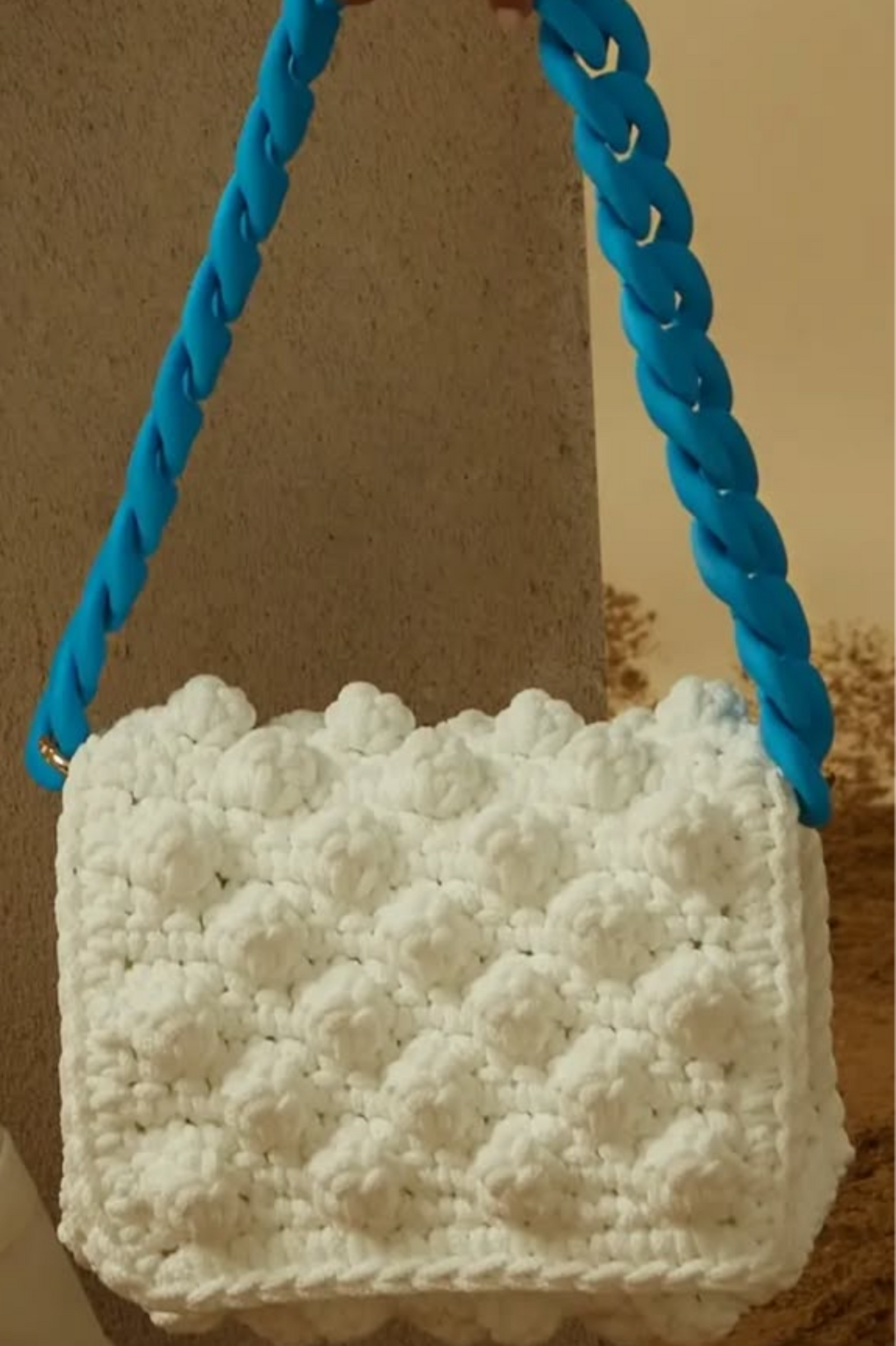 A hand crocheted white bag with a blue silicon chain, medium in size, from the '90s Collection'. The bag is displayed in a person's hand.