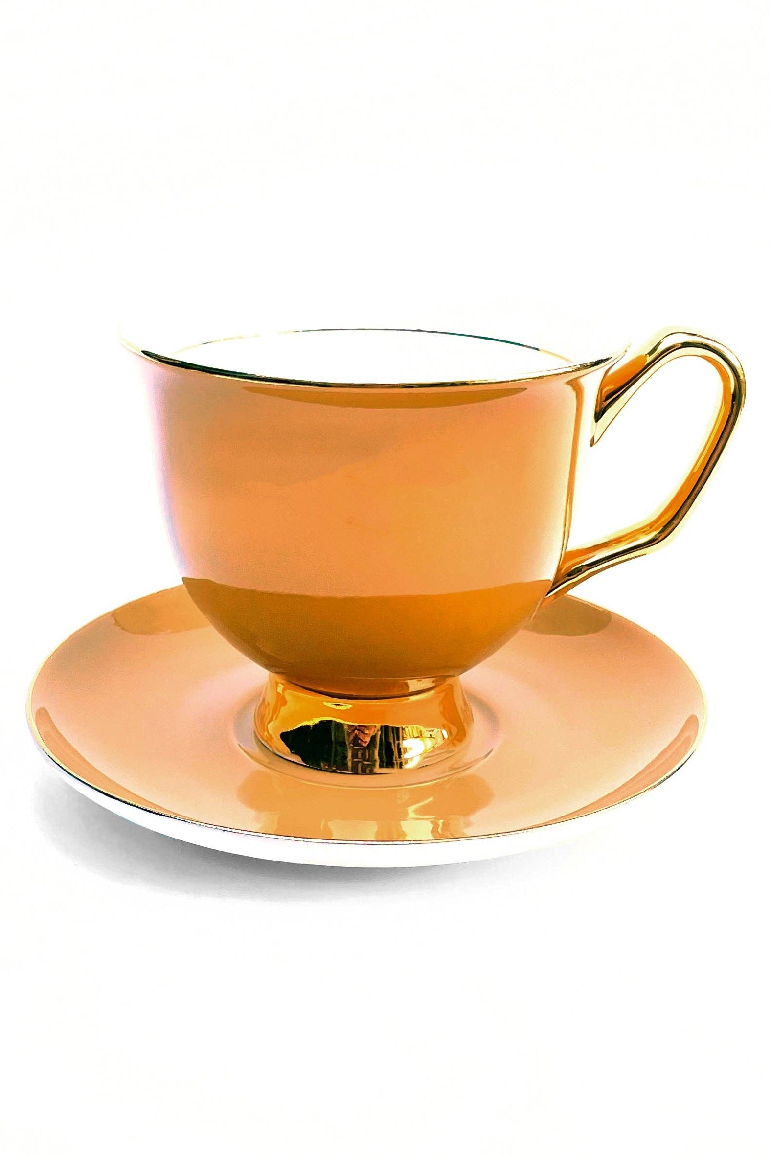 Orange teacup with gold handle and trim on a matching saucer against a white background