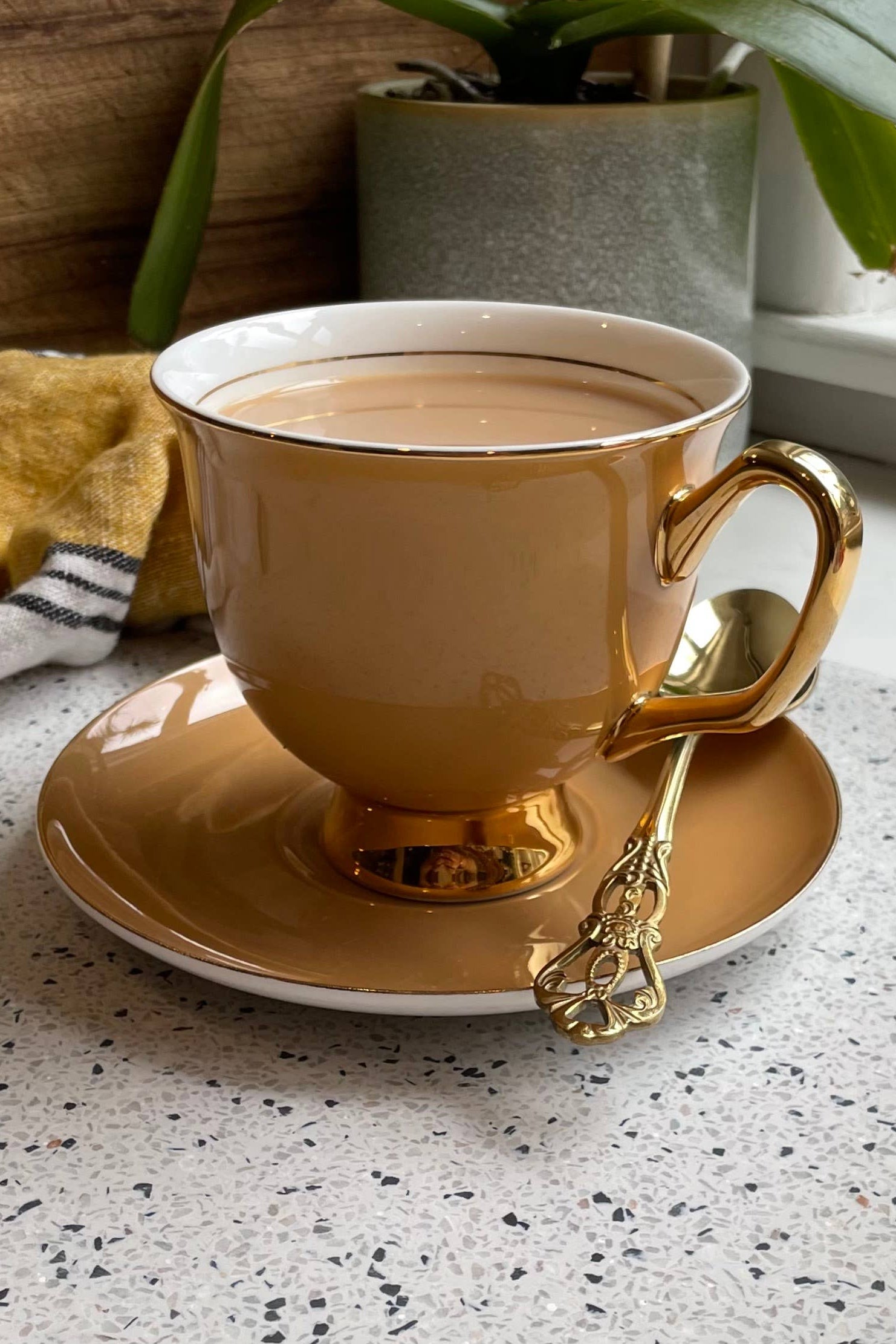 Orange teacup with gold handle and trim on a matching saucer against a white background