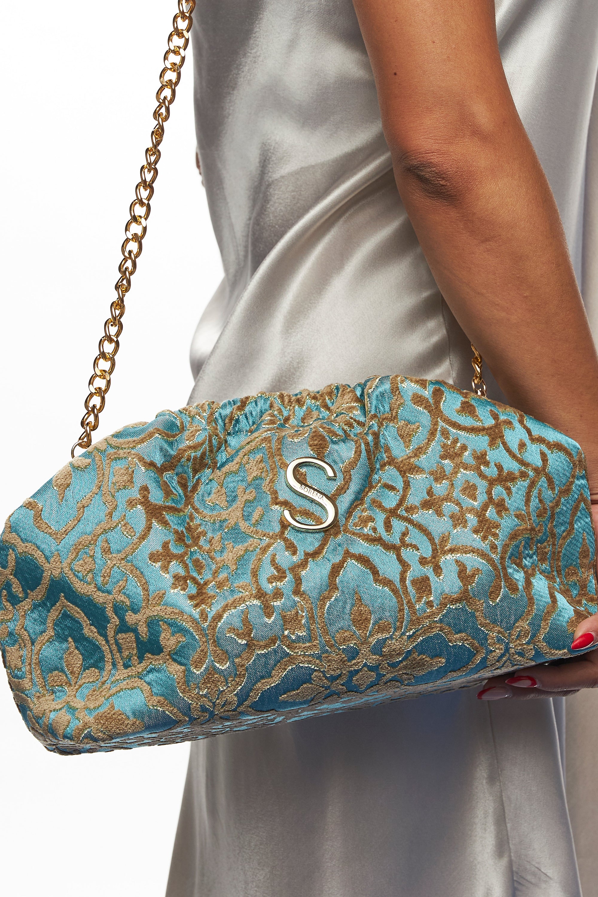 Blue and gold patterned clutch bag held by a person wearing a white dress.