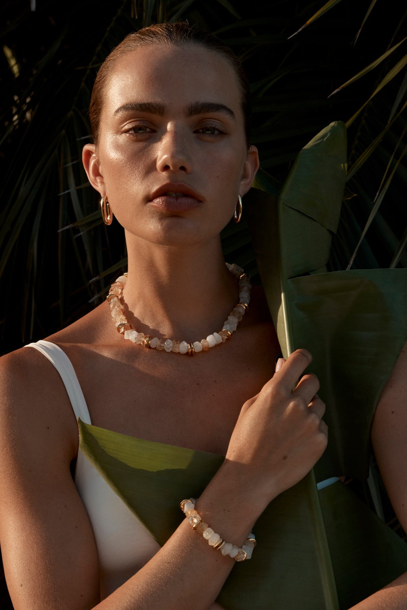 A person wearing the Yarrow Earrings, which are gold-colored with rectangular hoops, paired with a matching necklace and bracelet.