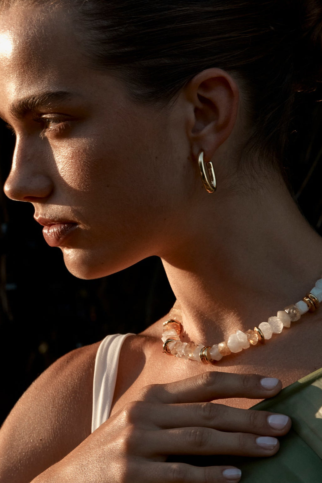 A person wearing the Yarrow Earrings, which are gold-colored with rectangular hoops, paired with a matching necklace and bracelet.