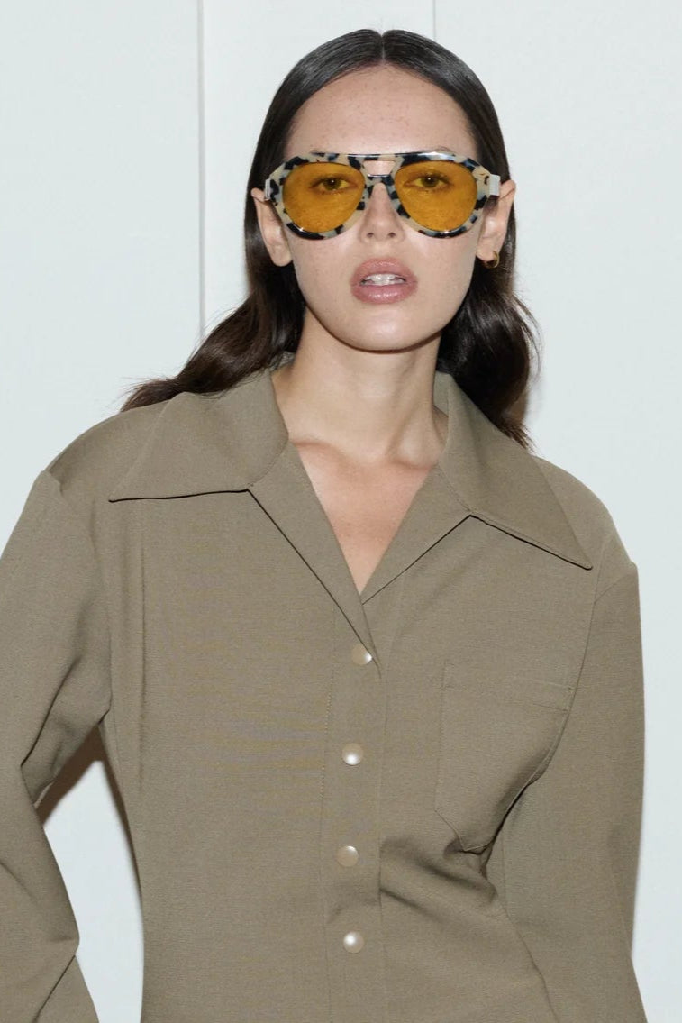 Woman wearing a beige trench coat and sunglasses against a white background
