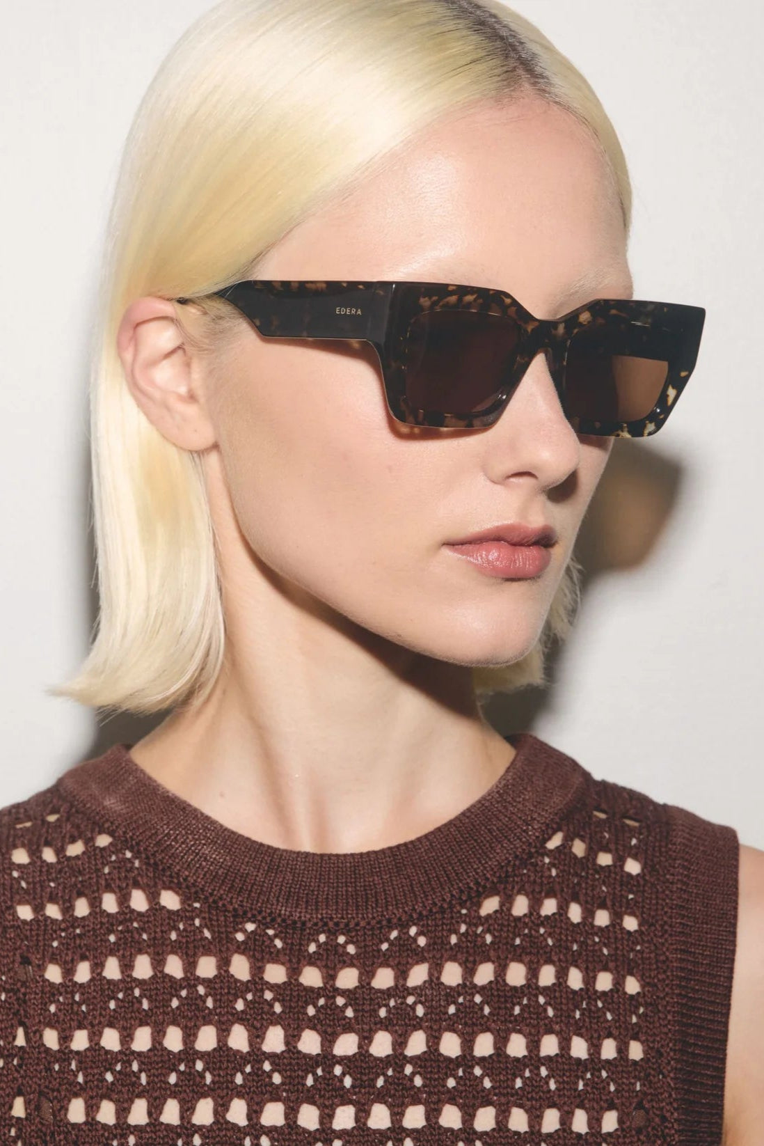 Woman wearing a patterned sleeveless top and sunglasses against a plain background
