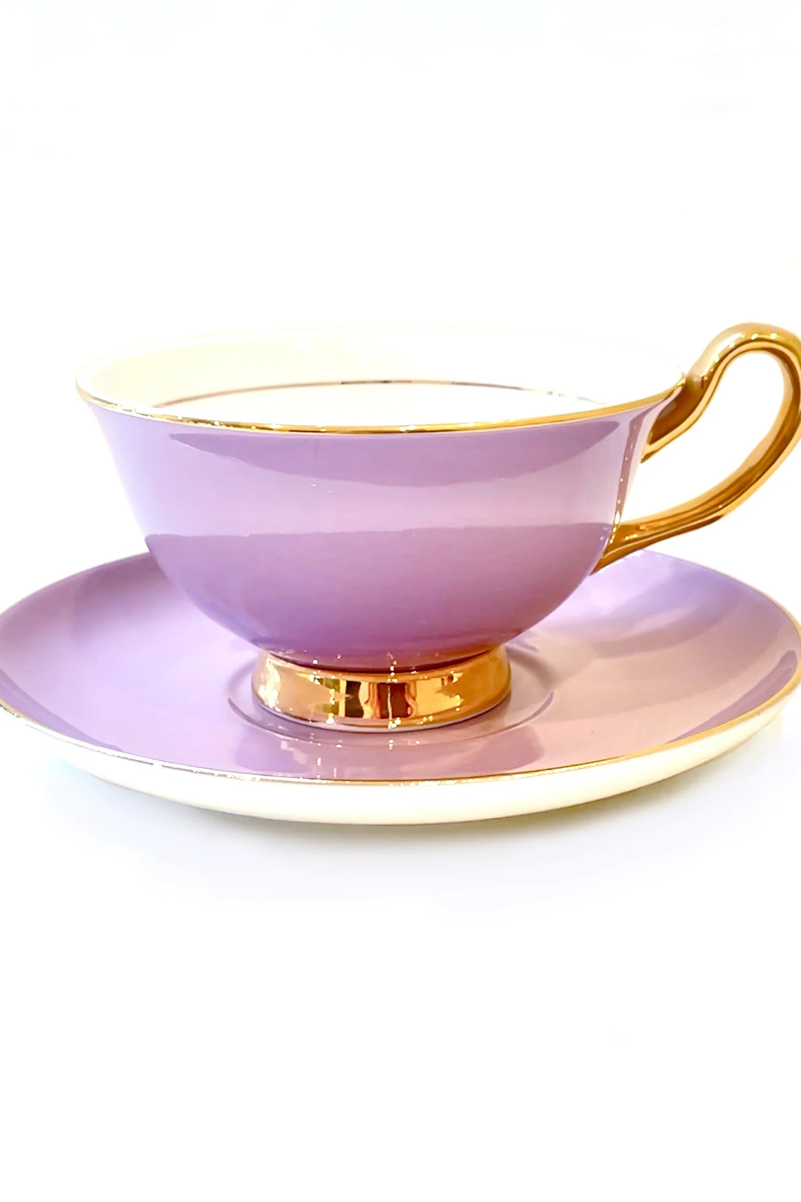A lavender colored teacup with gold trim and a matching saucer, both made of porcelain.