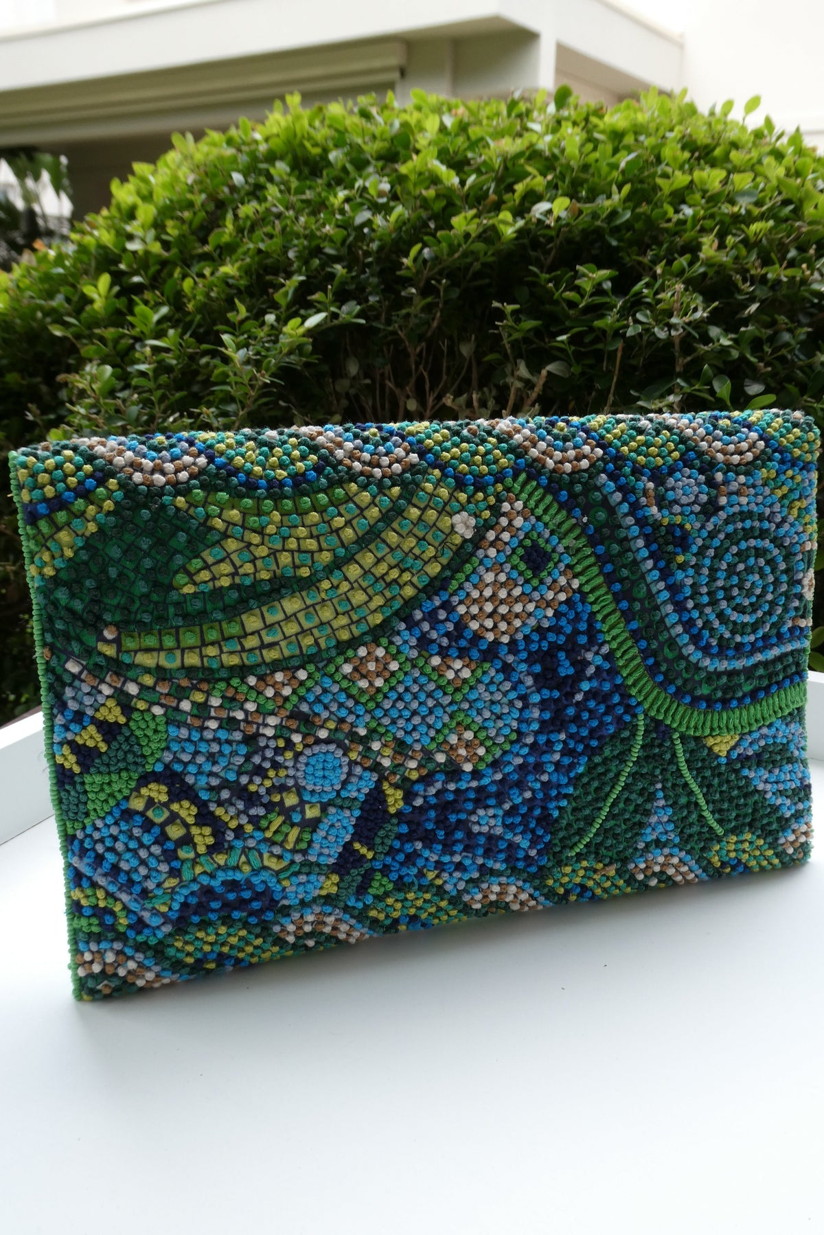 Decorative pillow with peacock pattern on a white surface next to a green plant