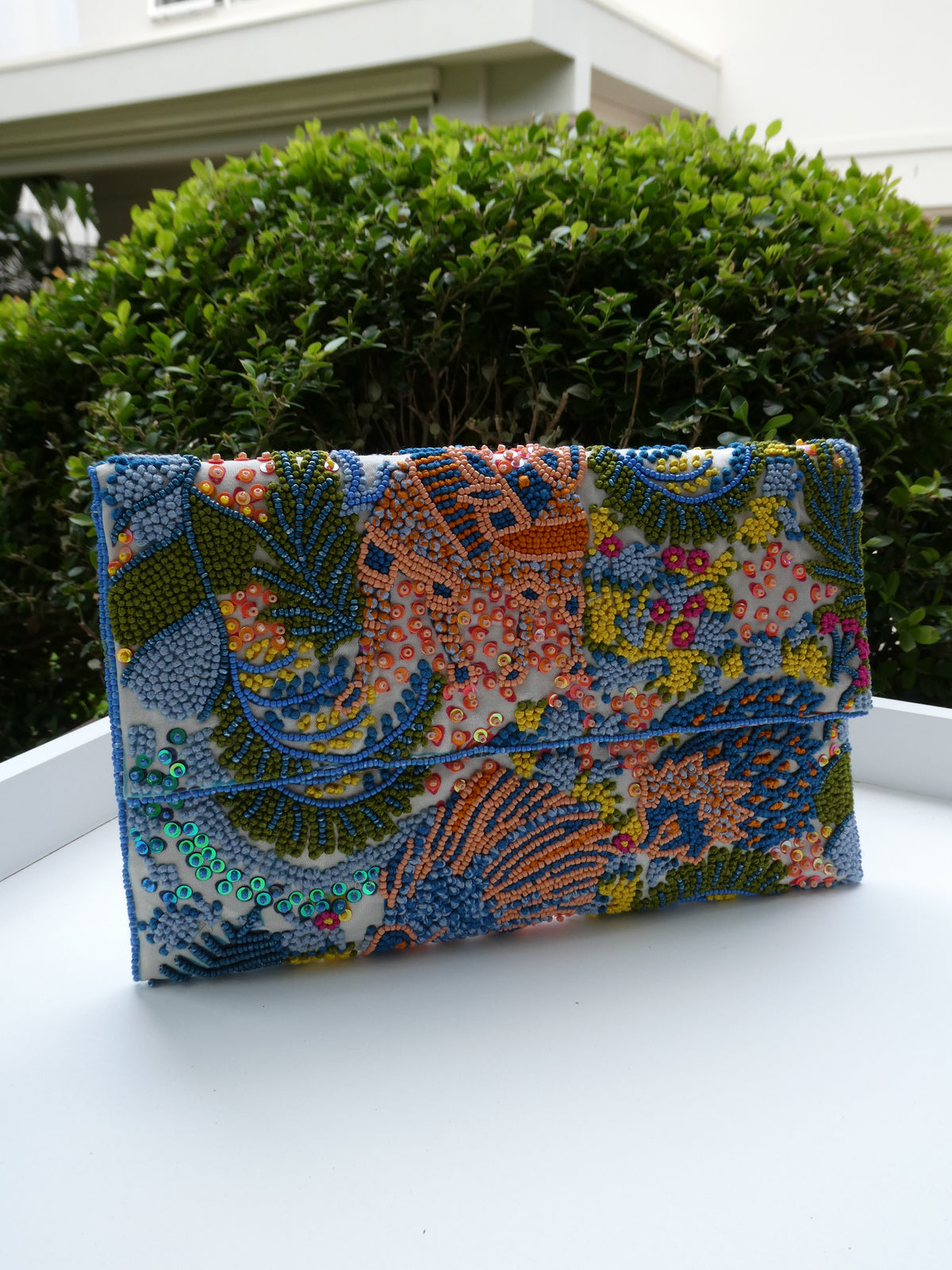 Colorful beaded clutch on a white surface with greenery in the background