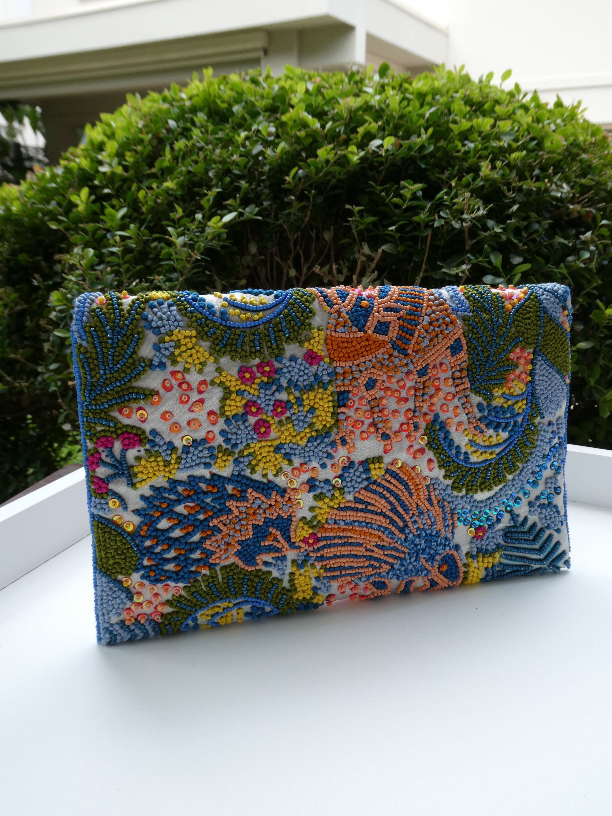 Colorful beaded clutch on a white surface with greenery in the background