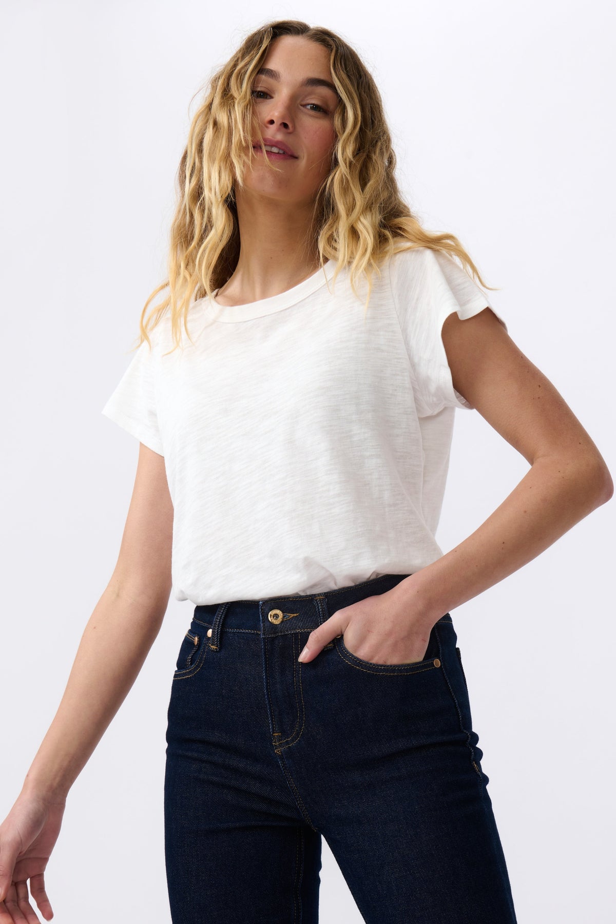 Woman wearing a white t-shirt and dark jeans on a plain background
