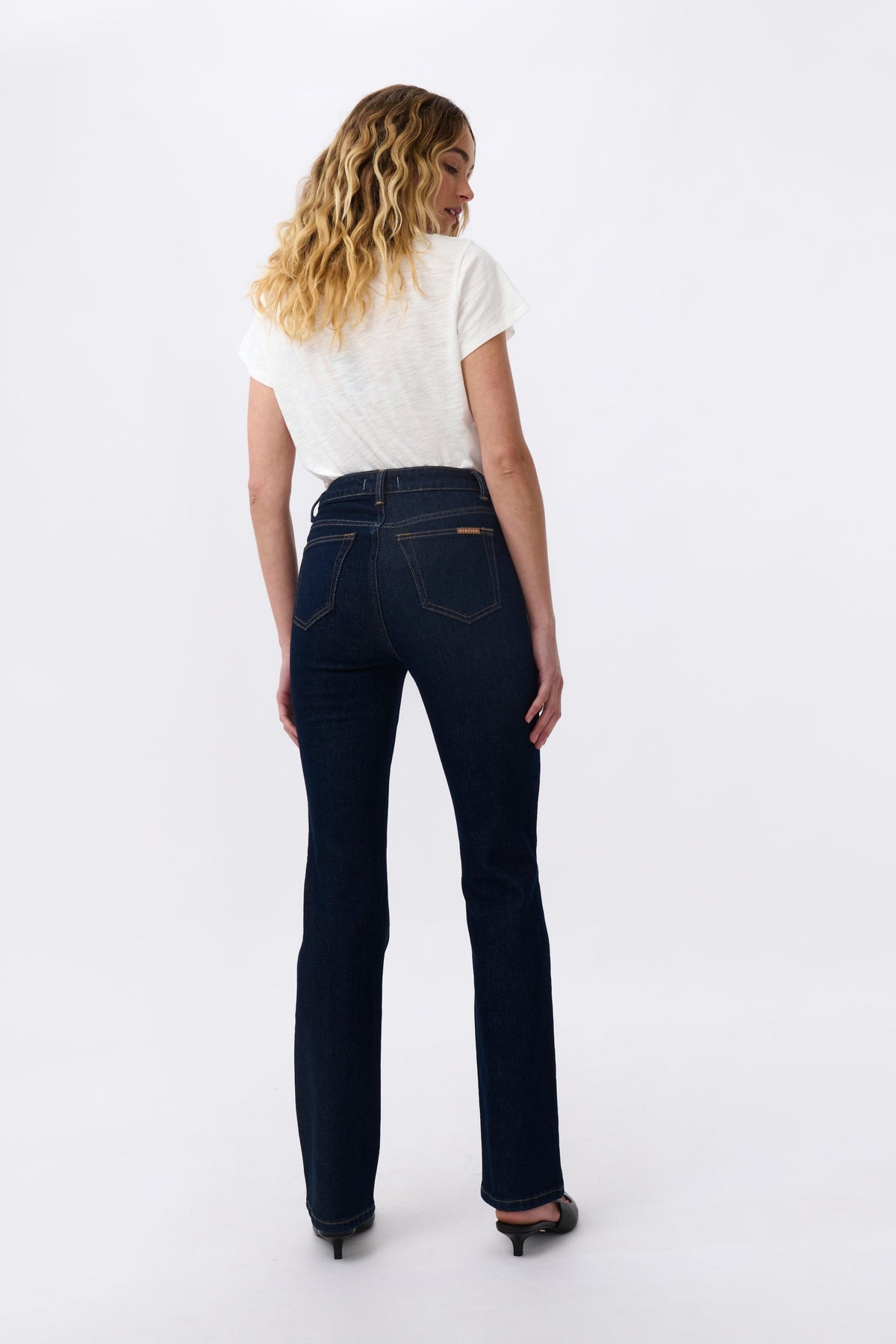 Woman wearing dark blue jeans and a white shirt on a light gray background