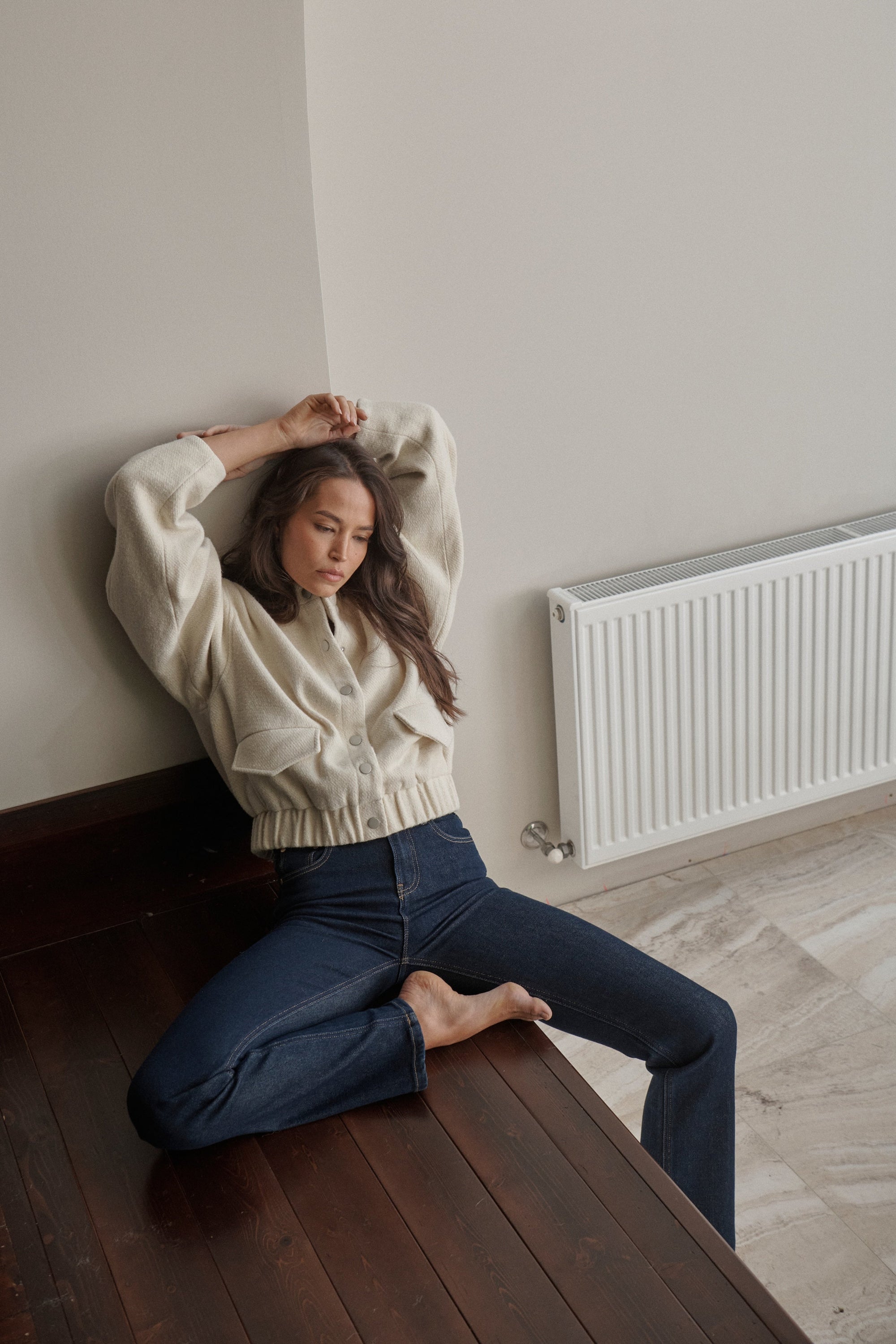 Woman sitting on a wooden bench against a wall with a radiator in the background