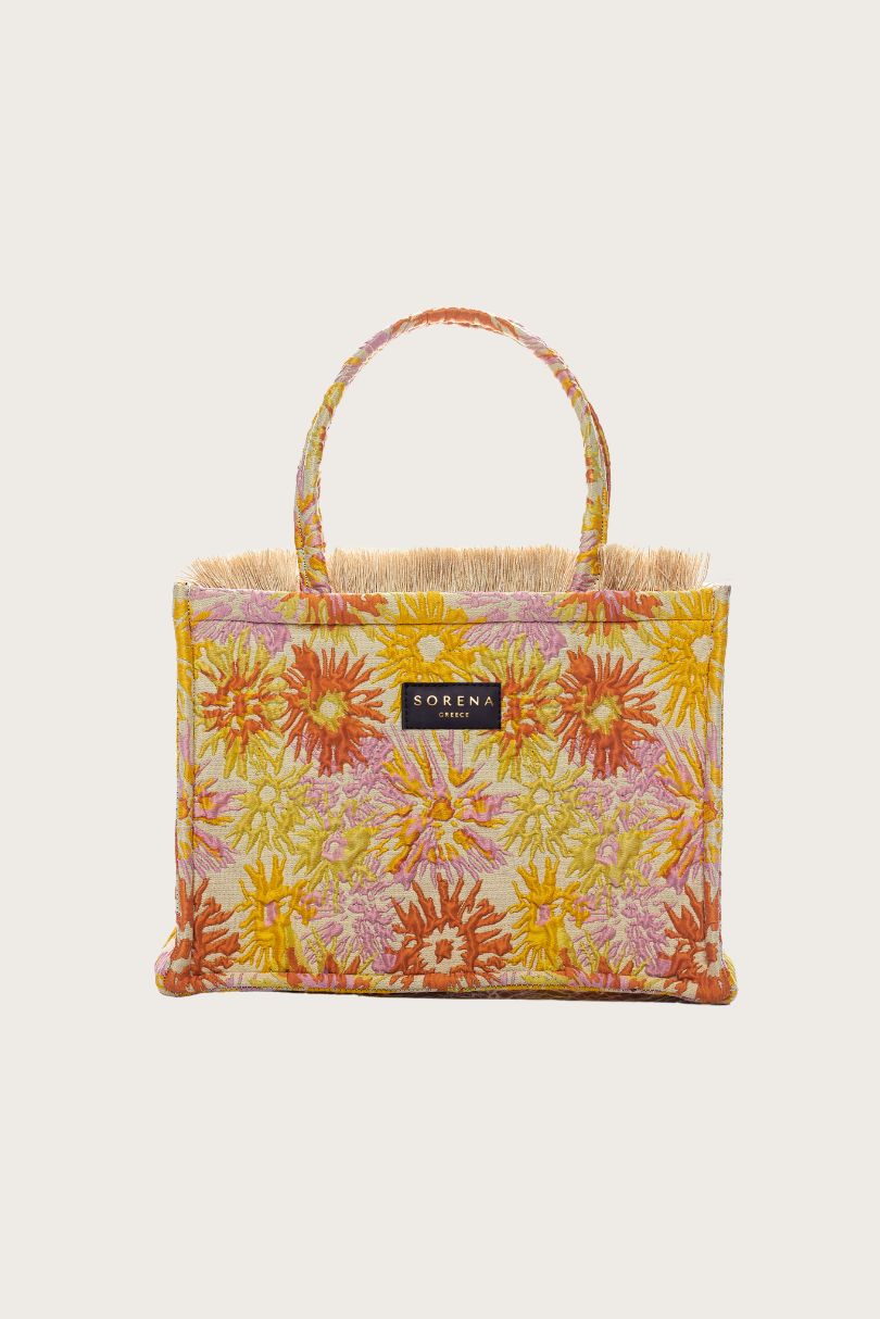 Floral patterned bag on a rock with ocean in the background, featuring the brand 'Sorena'.