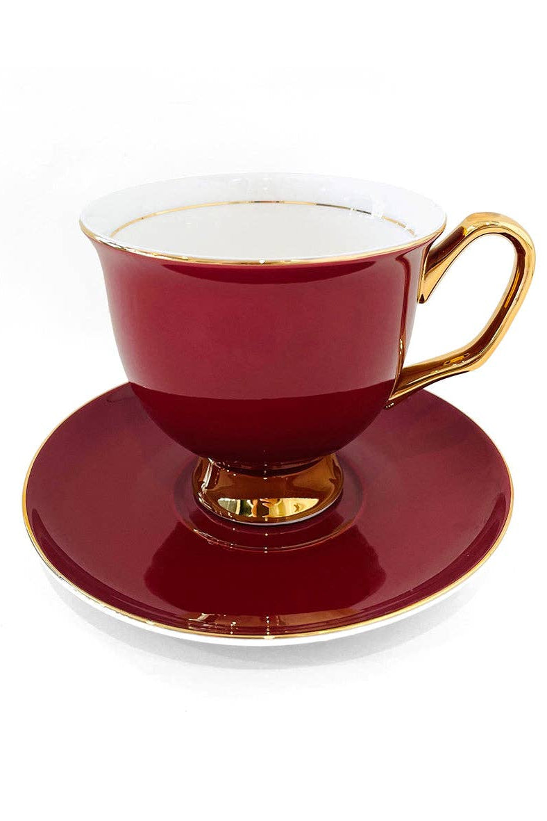 Red teacup and saucer with gold trim on a white background