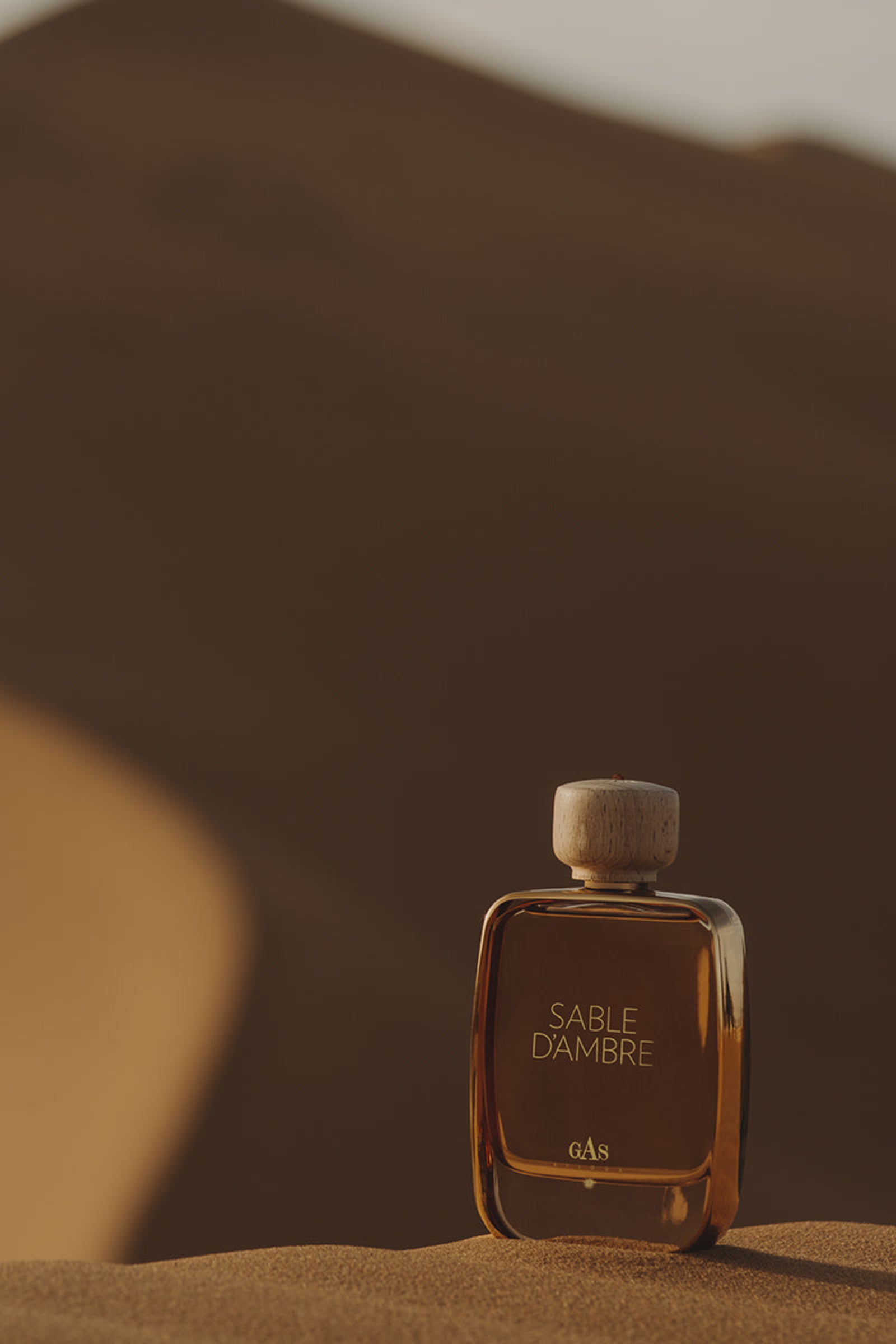 Perfume bottle labeled 'Sable Dámber' on sand dunes